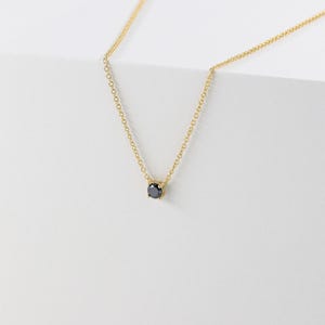 May include: A delicate gold necklace featuring a small, round, black gemstone pendant. The chain is fine and the pendant is set in a simple, minimalist style. The necklace is displayed against a white background.