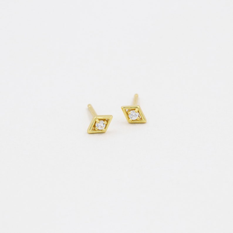 May include: A pair of gold diamond-shaped earrings with a small clear stone in the centre of each.
