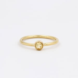 May include: A simple gold band ring with a small, round, yellow gemstone in the center.