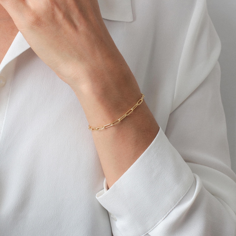 Puede incluir: Un brazalete de cadena dorada con un dise&ntilde;o simple y enlazado. El brazalete se lleva en la mu&ntilde;eca.