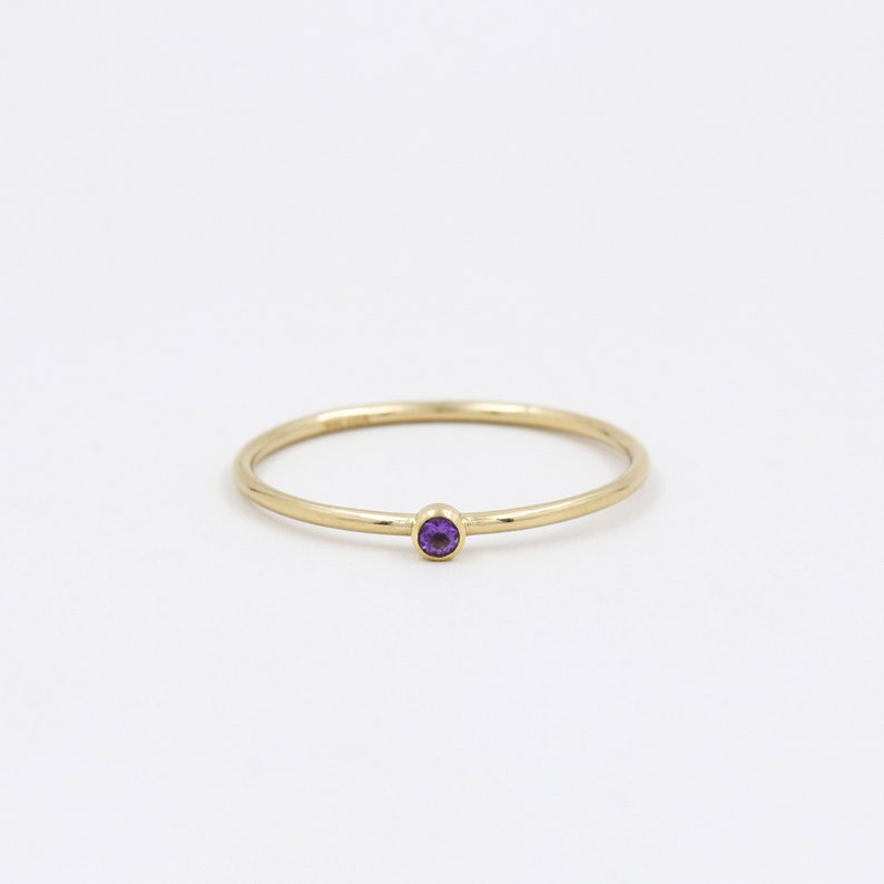 May include: A simple gold band ring with a small, round, purple amethyst gemstone.
