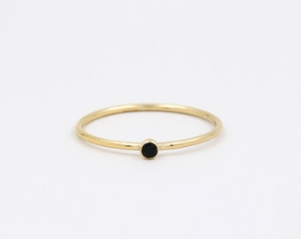 May include: A simple gold band ring with a small black stone in the center.