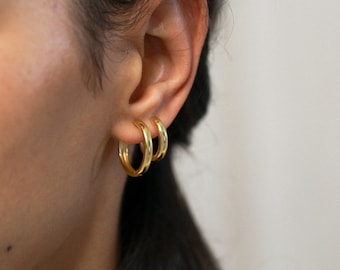 May include: A close-up of a person's ear wearing three gold hoop earrings of different sizes.