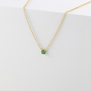 May include: A delicate gold chain necklace with a small, round green gemstone pendant.