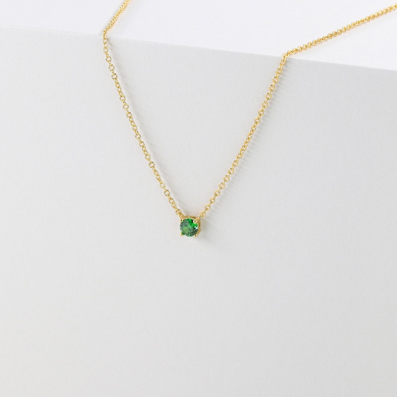 May include: A delicate gold chain necklace with a small, round green gemstone pendant.