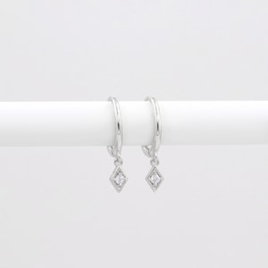 May include: A pair of silver hoop earrings with a small diamond-shaped pendant hanging from each hoop. The pendants have a single clear stone in the centre.