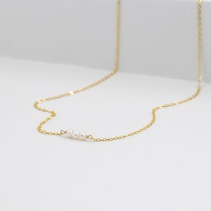 Puede incluir: Un delicado collar de cadena dorada con tres peque&ntilde;as perlas blancas.