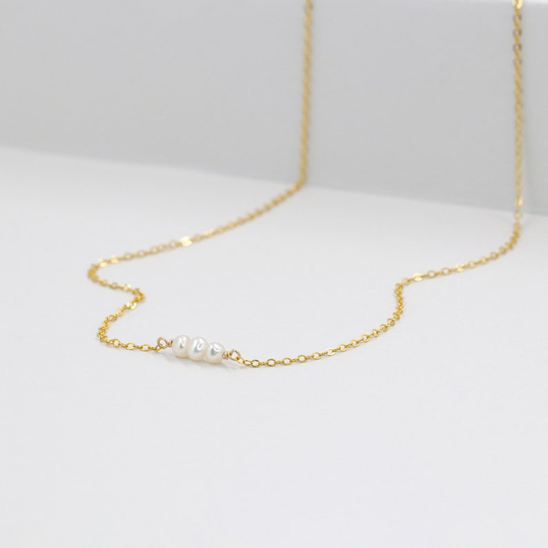 Puede incluir: Un delicado collar de cadena dorada con tres peque&ntilde;as perlas blancas.