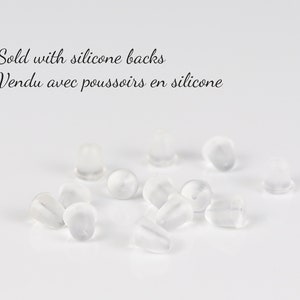 May include: A close-up of a pile of clear silicone earring backs. The text "Sold with silicone backs Vendu avec poussoirs en silicone" is visible in the image.