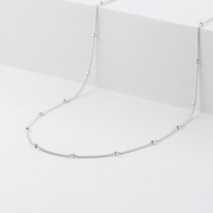 May include: A silver chain necklace with small round beads.