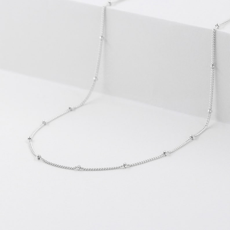 May include: A silver chain necklace with small round beads.