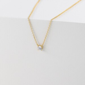May include: A delicate gold chain necklace with a single, clear round gemstone pendant.