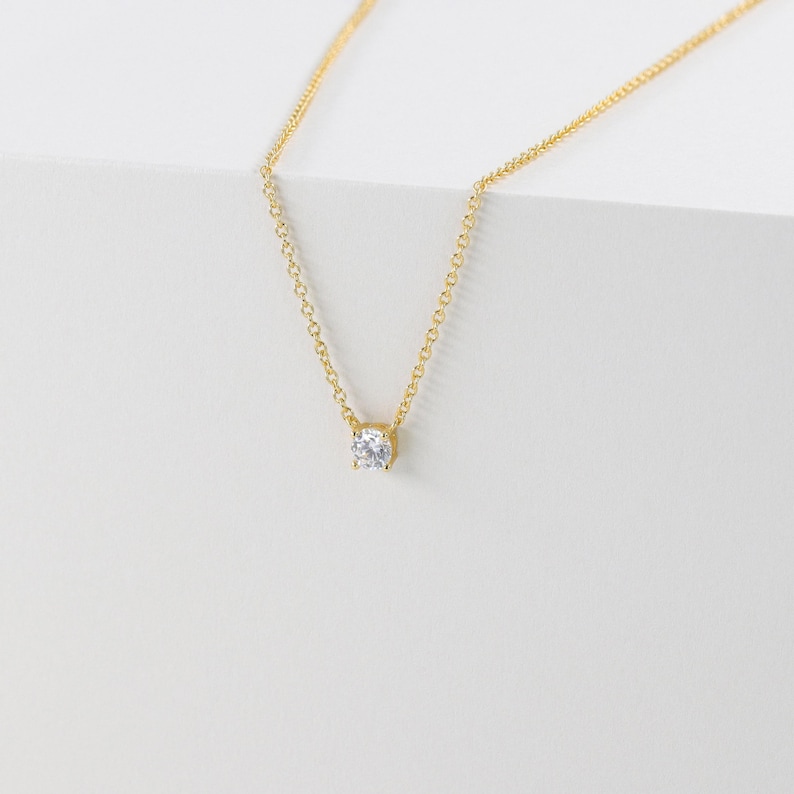 May include: A delicate gold chain necklace with a single, clear round gemstone pendant.
