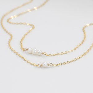 Puede incluir: Un delicado collar de cadena dorada con un dije de perla &uacute;nico y una fila de tres perlas.