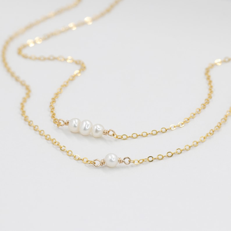 Puede incluir: Un delicado collar de cadena dorada con un dije de perla &uacute;nico y una fila de tres perlas.