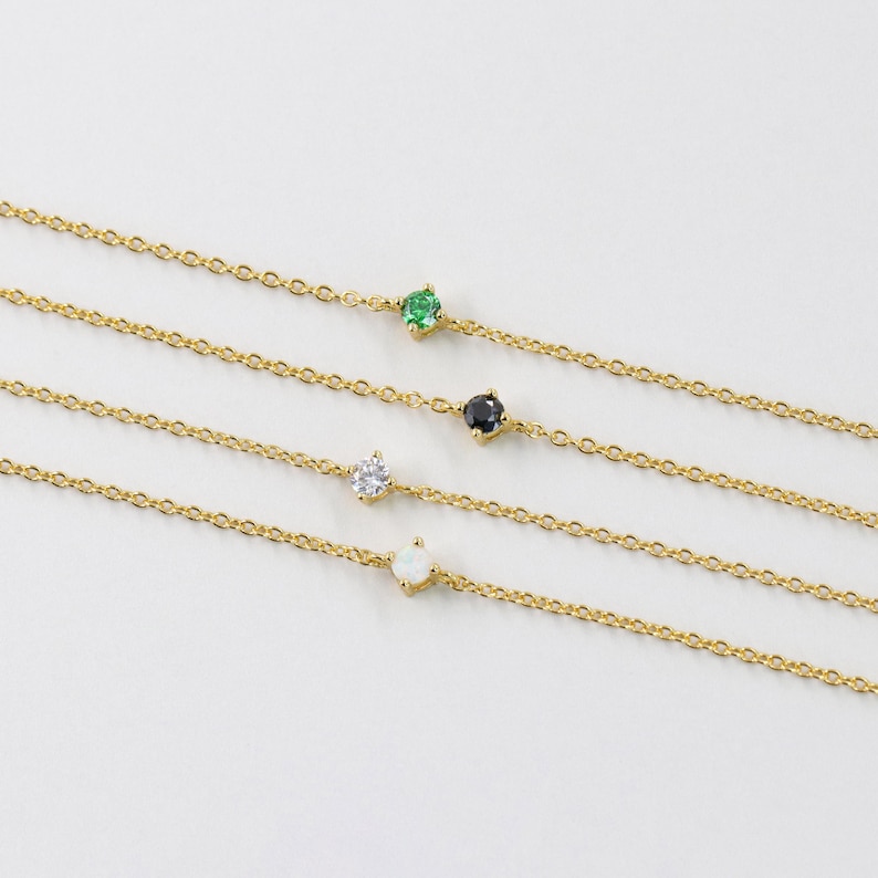 Pu&ograve; includere: Quattro delicati braccialetti a catena d'oro con un singolo accento di pietra preziosa su ciascuno. I braccialetti presentano una pietra preziosa verde, nera, bianca e opale.