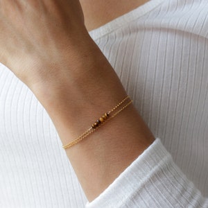 May include: A gold chain bracelet with a small strand of tiger's eye beads.