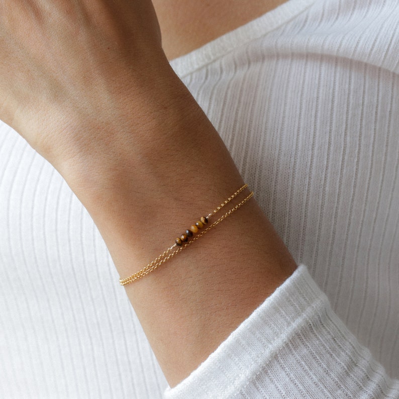 May include: A gold chain bracelet with a small strand of tiger's eye beads.