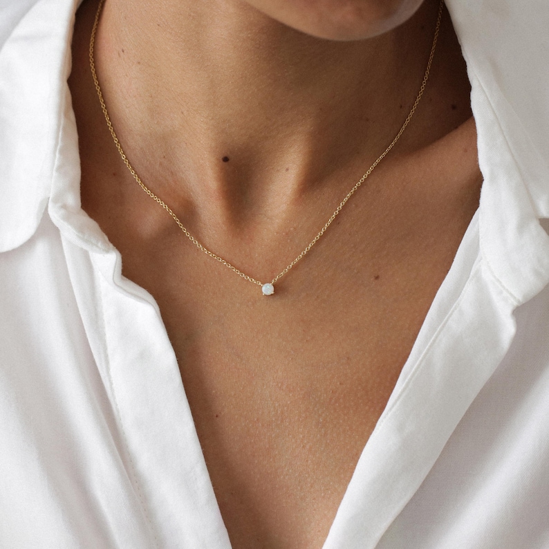 May include: A delicate gold chain necklace with a small, round, white gemstone pendant.