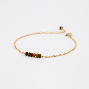 May include: A gold chain bracelet with a row of tiger's eye beads.