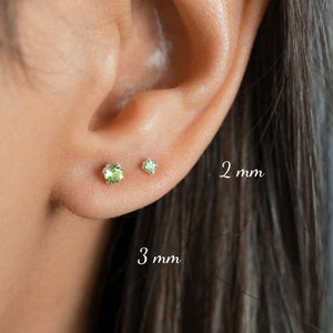 May include: Close-up of a person's ear with two green gemstone earrings. The earring on the left is 3 mm and the earring on the right is 2 mm.