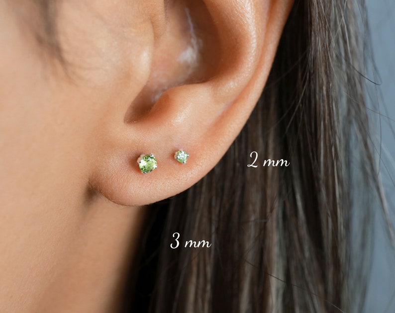 May include: Close-up of a person's ear with two green gemstone earrings. The earring on the left is 3 mm and the earring on the right is 2 mm.