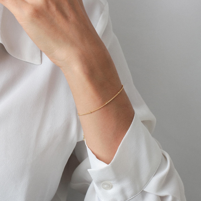 Puede incluir: Un delicado brazalete de cadena dorada con un sutil dise&ntilde;o de cuentas. El brazalete se lleva en la mu&ntilde;eca.
