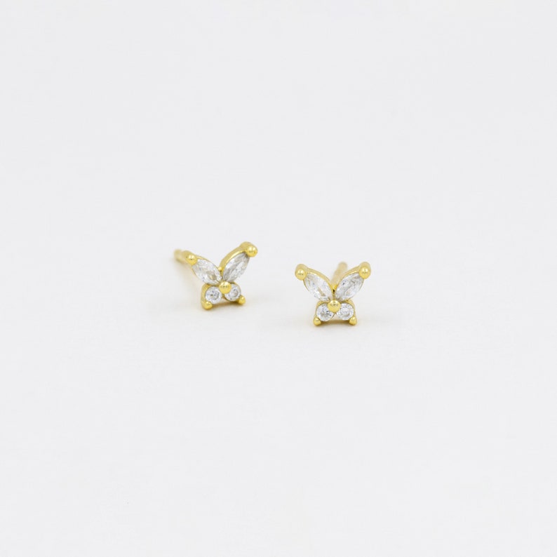 May include: A pair of gold butterfly earrings with clear cubic zirconia stones.