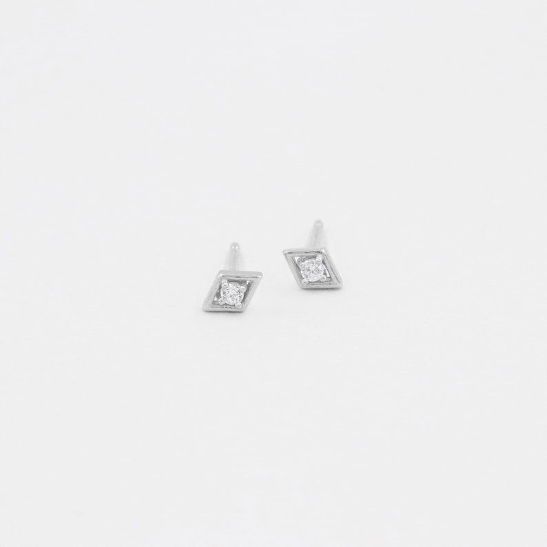 May include: A pair of silver diamond earrings with a small diamond in the centre of each earring.