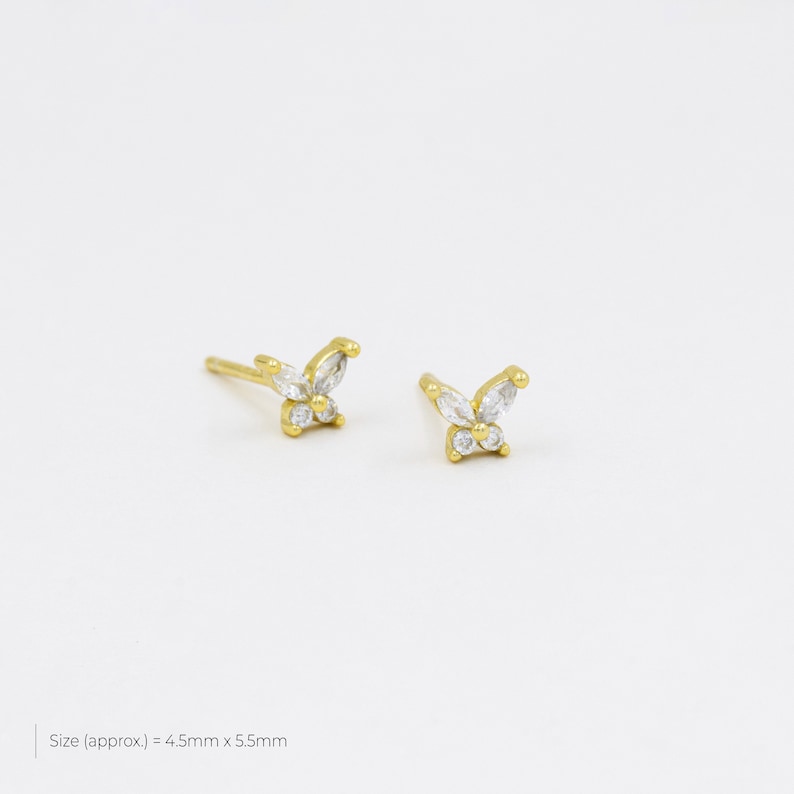 May include: A pair of gold butterfly earrings with clear cubic zirconia stones. The earrings are approximately 4.5mm x 5.5mm in size.