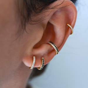 May include: A close-up of a person's ear with multiple gold hoop earrings. The earrings are adorned with small black and white stones.