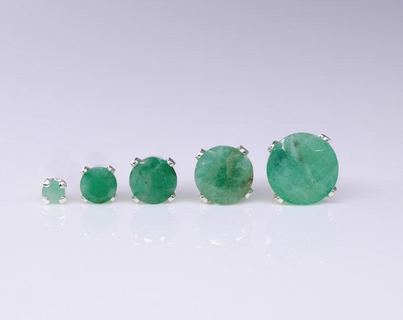 May include: Four emerald green gemstone earrings in silver settings, arranged in order of size from smallest to largest.
