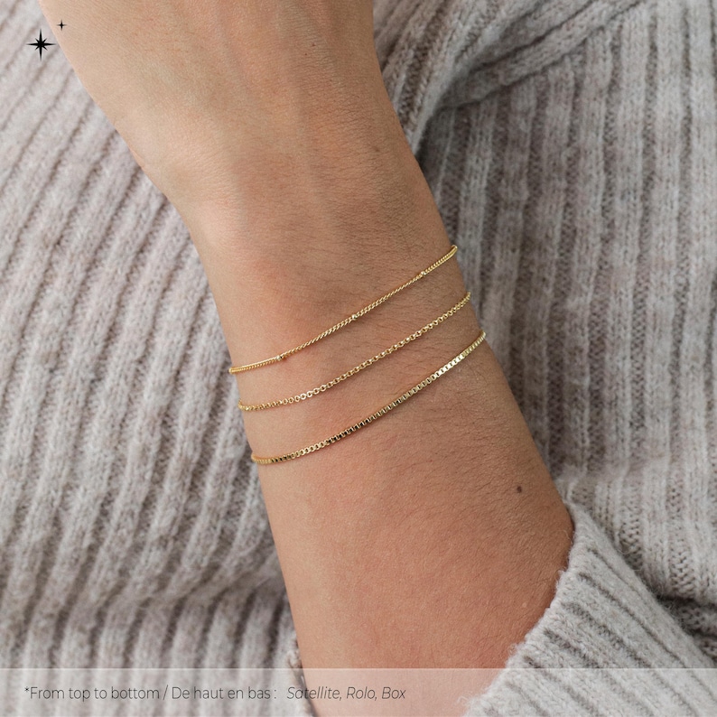 Puede incluir: Tres pulseras de cadena de oro apiladas en la mu&ntilde;eca de una persona. Las pulseras son, de arriba a abajo: Satellite, Rolo y Box.