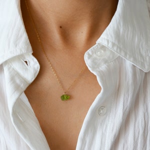 Peut inclure: Un collier délicat en chaîne dorée avec un petit pendentif en pierre précieuse verte.