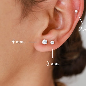 Pu&ograve; includere: Primo piano di un orecchio con tre diverse dimensioni di orecchini a perno. Gli orecchini hanno un diametro di 2 mm, 3 mm e 4 mm.