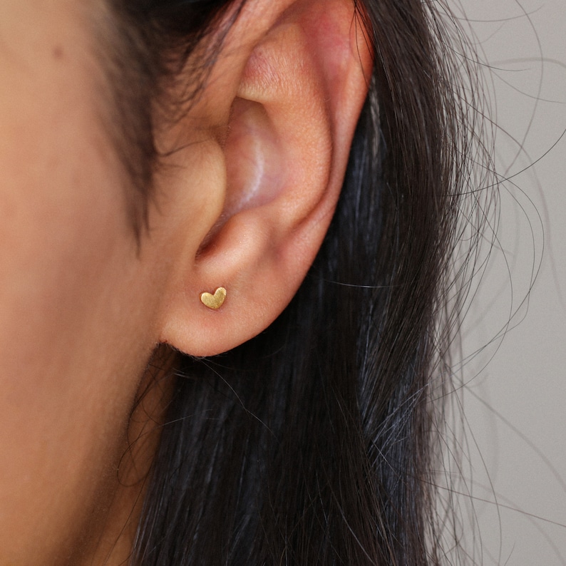 May include: A close-up of a person's ear with a small gold heart-shaped stud earring.