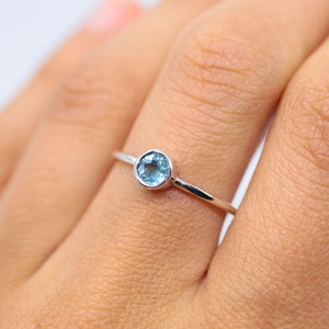 May include: A silver ring with a light blue gemstone. The ring is on a person's finger.