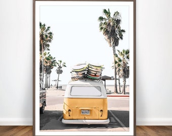 May include: A framed print featuring a yellow and white vintage van with surfboards stacked on top. The van is parked on a street lined with palm trees, with a beach and ocean in the background. The image has a bright, sunny aesthetic.