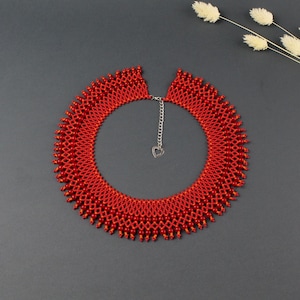 Può includere: Una collana di perline rosse con una chiusura a forma di cuore argentata. La collana è realizzata con piccole perline rotonde disposte in un motivo graduato, creando un effetto a cascata. La collana è un pezzo di dichiarazione che aggiungerebbe un tocco di eleganza a qualsiasi outfit.