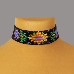 May include: A black beaded choker necklace with a floral design. The choker features a repeating pattern of colorful flowers in shades of yellow, blue, green, and purple. The necklace is displayed on a yellow mannequin.