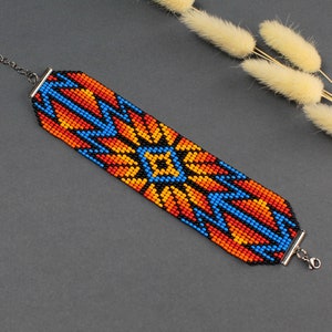 May include: A beaded bracelet with a geometric pattern in shades of orange, blue, and black. The bracelet has a silver clasp.