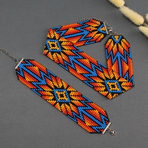 Puede incluir: Un conjunto de dos collares de cuentas con un patrón geométrico en tonos naranja, azul y negro. Los collares están hechos con cuentas pequeñas y tienen cierres plateados.