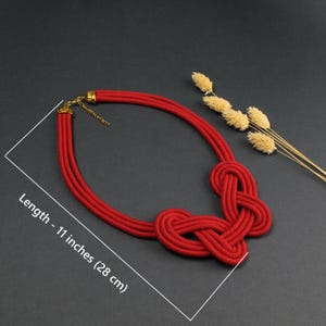 Pode incluir: Um colar de corda vermelha com um design de n&oacute;s. O colar tem aproximadamente 28 cm de comprimento. O colar tem um fecho e uma corrente dourados. O fundo &eacute; escuro.