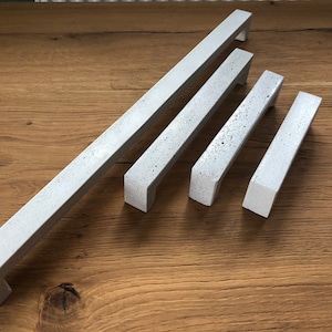May include: Four concrete cabinet pulls in various sizes. The pulls are a light gray color with a rough texture.