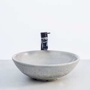 May include: A round, gray concrete sink with a black faucet.