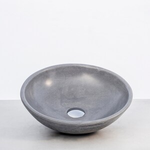 May include: A gray ceramic vessel sink with a round, bowl-shaped design. The sink has a smooth, slightly textured surface and a small drain hole in the center.