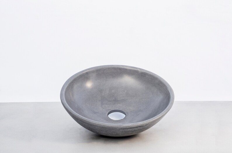 May include: A gray ceramic vessel sink with a round, bowl-shaped design. The sink has a smooth, slightly textured surface and a small drain hole in the center.