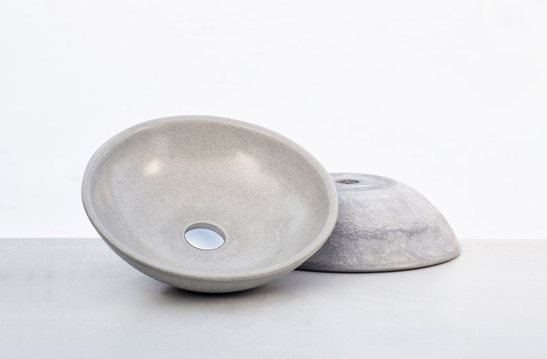 May include: Two gray ceramic bowls, one with a drain hole, are sitting on a gray surface. The bowls are both round and have a smooth, slightly textured surface.