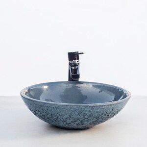 May include: A gray ceramic vessel sink with a textured surface and a black faucet.