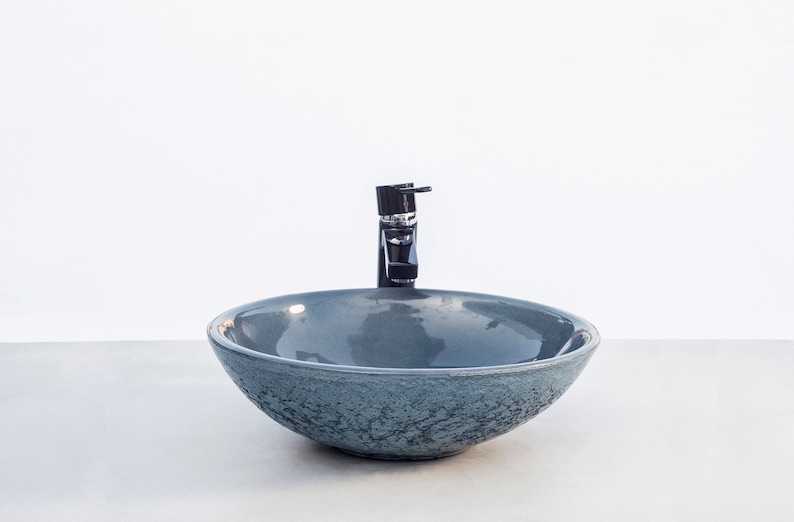 May include: A gray ceramic vessel sink with a textured surface and a black faucet.